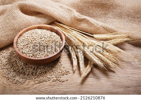 Bowl of rye grains and ears on wooden table