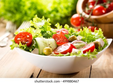 bowl of salad with vegetables and greens on wooden table
