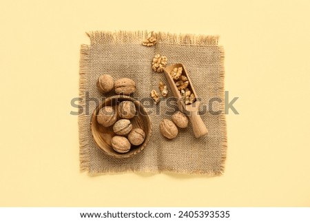 Bowl and scoop of tasty walnuts on yellow background