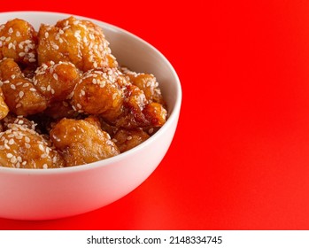 Bowl Of Sesame Chicken On A Bright Red Background