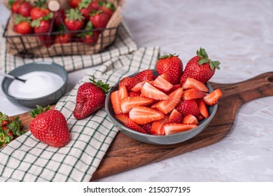 Bowl of sliced strawberries on a board and a small bowl of sugar, basket of fresh fruit - Powered by Shutterstock