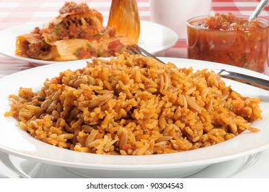 A Bowl Of Spanish Or Mexican Rice With Tamales In The Background