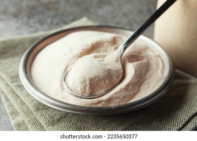 Bowl and spoon of agar-agar powder on grey table, closeup