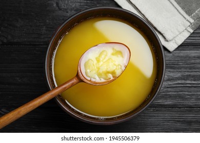 Bowl and spoon of Ghee butter on dark wooden table, flat lay