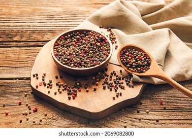 Bowl and spoon with mixed peppercorns on wooden background