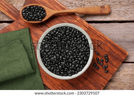 Bowl and spoon of raw black beans on wooden table, flat lay