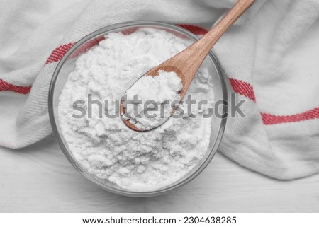 Bowl and spoon of starch on white wooden table, top view