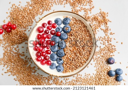 Bowl of sweet yogurt with flax seeds and berries on light background