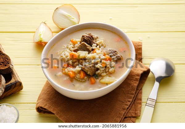 Bowl with tasty beef barley soup on color\
wooden background