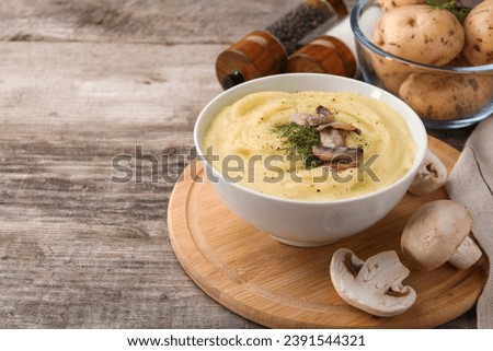 Bowl of tasty cream soup with fried mushrooms, dill and raw potatoes on wooden table. Space for text