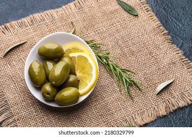 Bowl of tasty green olives, lemon slices and rosemary on table - Powered by Shutterstock