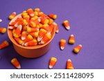 Bowl of tasty Halloween candy corns on purple background