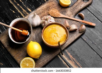 Bowl of tasty honey mustard sauce with ingredients on dark wooden background