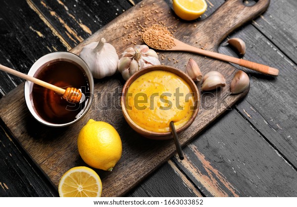 Bowl of tasty honey mustard sauce with\
ingredients on dark wooden\
background
