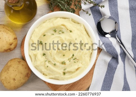 Bowl of tasty mashed potato with rosemary and olive oil on beige wooden table, flat lay