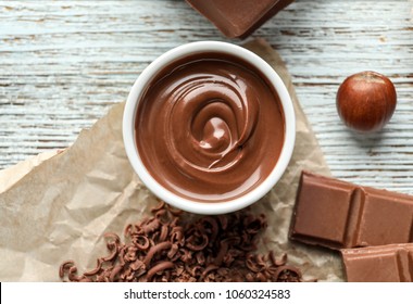 Bowl with tasty melted chocolate on wooden background