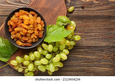 Bowl with tasty raisins and ripe grapes on wooden background