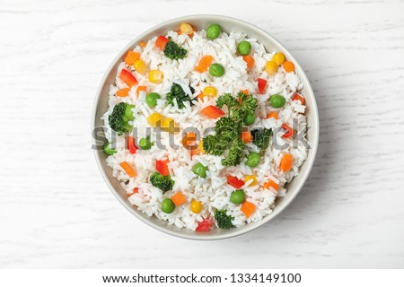 Bowl with tasty rice and vegetables on wooden background, top view