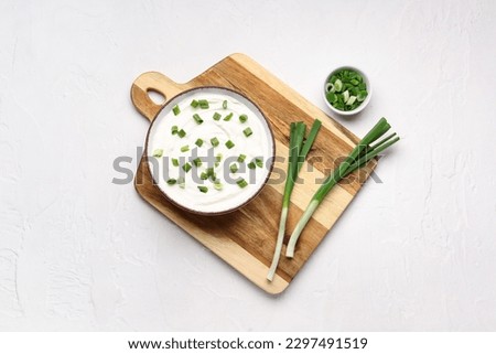 Bowl of tasty sour cream with green onion on light background