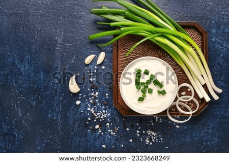Bowl of tasty sour cream with scallion and onion on blue background