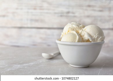 Bowl with tasty vanilla ice cream on table against light background