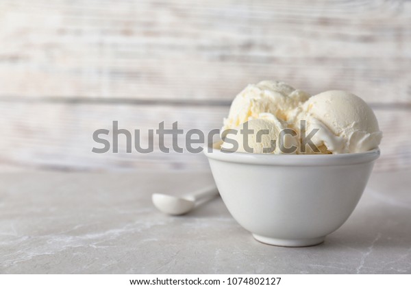Bowl with tasty vanilla ice cream on table\
against light background