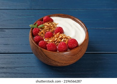 Bowl of tasty yogurt with raspberries and muesli served on blue wooden table