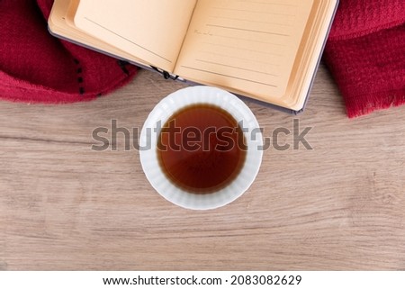 A bowl of tea and an open book and scarf