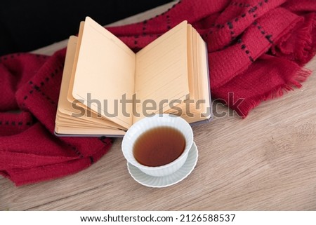 A bowl of tea and an open book and scarf