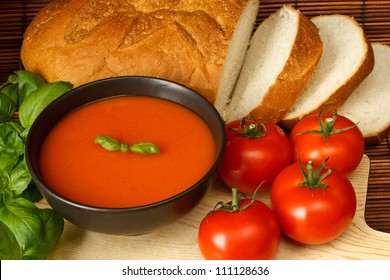 Bowl Of Tomato Soup With Basil Garnish, In Kitchen Setting Surrounded By Ingredients