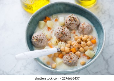 Bowl of turkish soup with chickpeas and meatballs, horizontal shot on a light-grey marble background