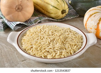 A Bowl Of Uncooked Orzo Pasta With Assorted Winter Squash In The Background