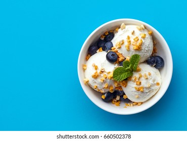 Bowl of vanilla ice cream with blueberries and mango pieces isolated on blue background. Top view