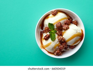 Bowl of vanilla ice cream, caramel sauce and nuts isolated on green background. Top view