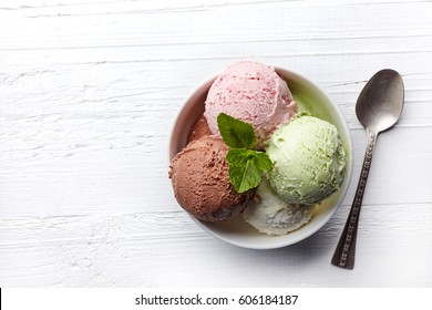Bowl of various colorful ice cream balls on white wooden background. From top view