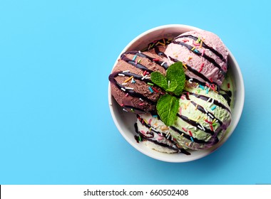 Bowl of various colorful ice cream and chocolate sauce isolated on blue background. Top view