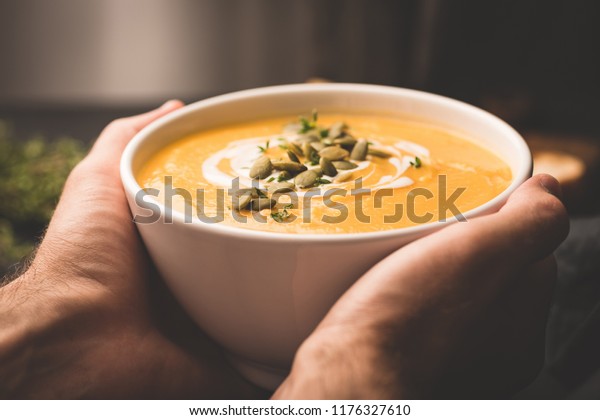 Bowl of warm\
pumpkin soup in hands. Holding bowl of vegan pumpkin soup. Comfort\
food. Toned image, selective\
focus
