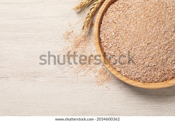 Bowl of wheat bran on white wooden table, flat lay.\
Space for text