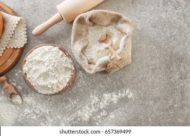 Bowl of wheat flour and sackcloth bag with scoop on light background