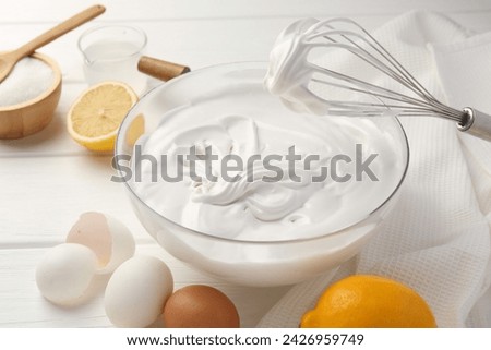 Bowl with whipped cream, whisk and ingredients on white wooden table