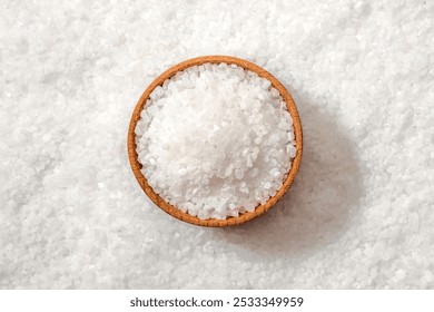 Bowl of white salt on salt background. Coarse sea salt, top view