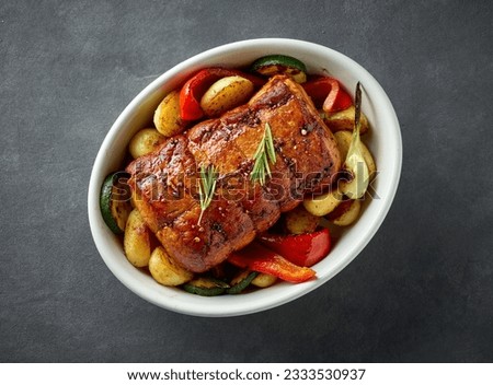 bowl of whole roast pork and vegetables on dark grey kitchen table, top view