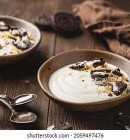 A bowl with yoghurt with bisquits on top on the wood background. 
