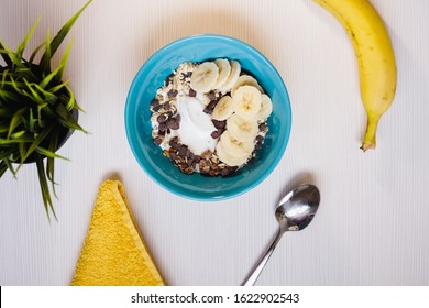 Bowl With Yummy Muesli, Yogurt And Banana Breakfast On White Background. Healthy Vegan Food Concept. Top Down View. Flat Lay.