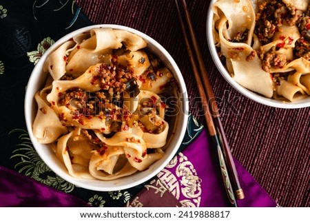 Bowls of Biang Biang Noodles Topped with Spicy Chili Oil Sauce: Biang biang mian topped with minced pork and chili oil served in bowls with chopsticks