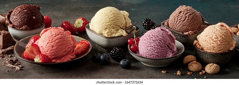 Bowls of craft ice cream with fresh ingredients including macaroons, variety of berries, vanilla pods and chocolate in a dark panorama banner
