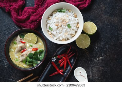 Bowls with green chicken curry and white rice over dark-brown stone background, top view, horizontal shot