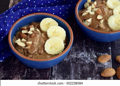 Bowls Of Homemade Oatmeal Spelt Porridge With Banana, Almonds And Almond Butter On Rustic Table, Healthy Food For Breakfast