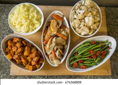 Bowls of Meal Side Dishes of Yellow Rice, Roasted Potatoes and Root Vegetables, Green Beans, and Tomatoes