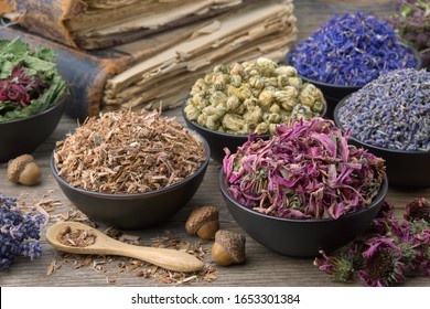 Bowls and mortars of dry medicinal herbs: lavender, cornflower, coneflower, daisies. Healing herbs assortment and old books on wooden table. Herbal medicine. 